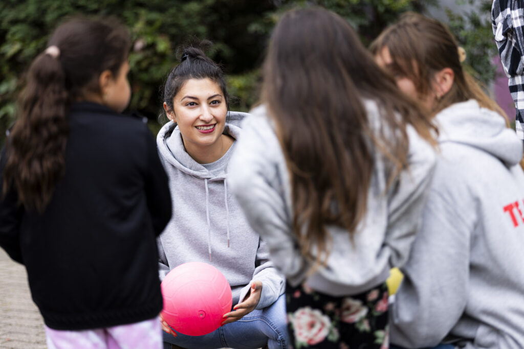 Zwei Erwachsene sprechen mit zwei Kindern. Eine Erwachsene hält einen pinken Ball in der Hand.