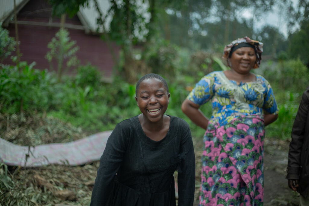 Ein Mädchen lacht. Hinter ihr steht ihr Betreuerin. Gemeinsam sind sie inmitten der Natur.
