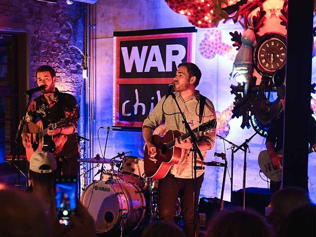 Eine Band spielt auf der Bühne vor einer War Child Flagge