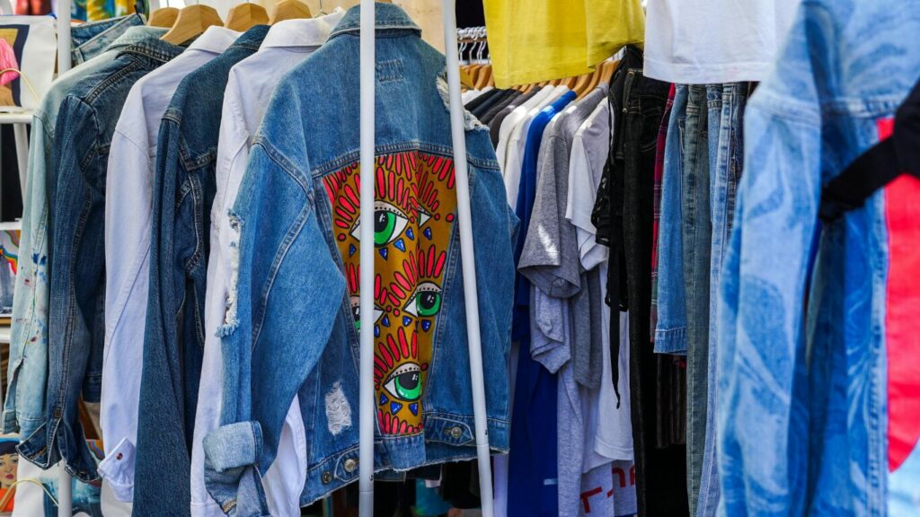 Eine Reihe von bunten Jeansjacken ist auf eine Kleiderstange eines Flohmarktstandes