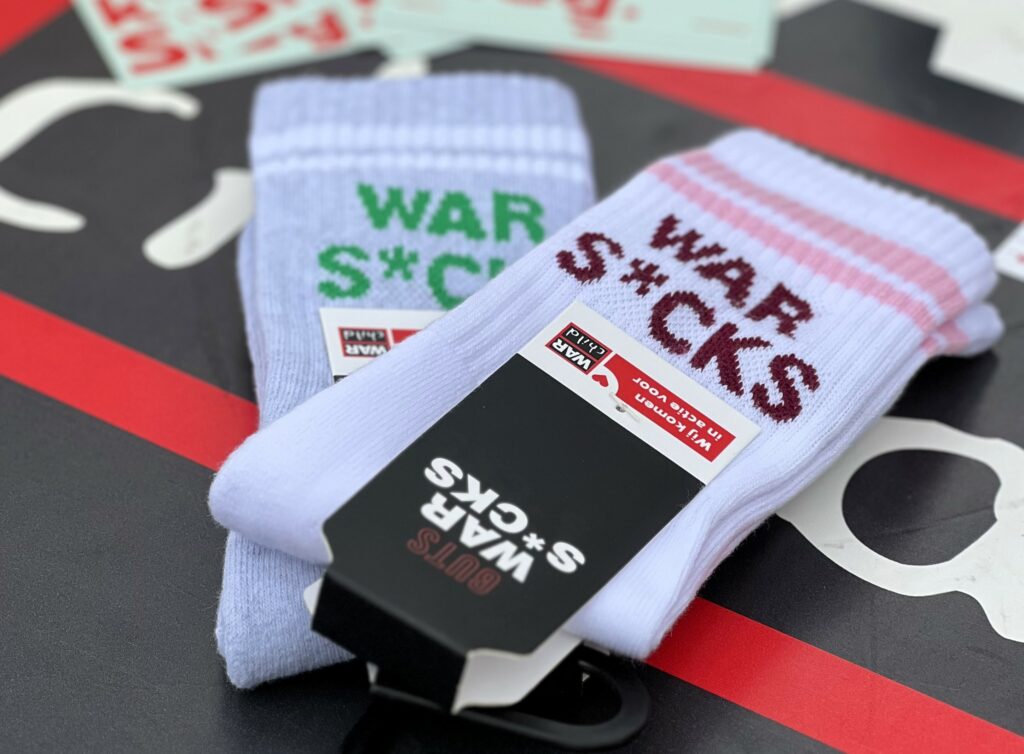 Zwei paar Socken liegen auf einem Tisch. Die Aufschrift ist auf den Socken ist War S*cks.