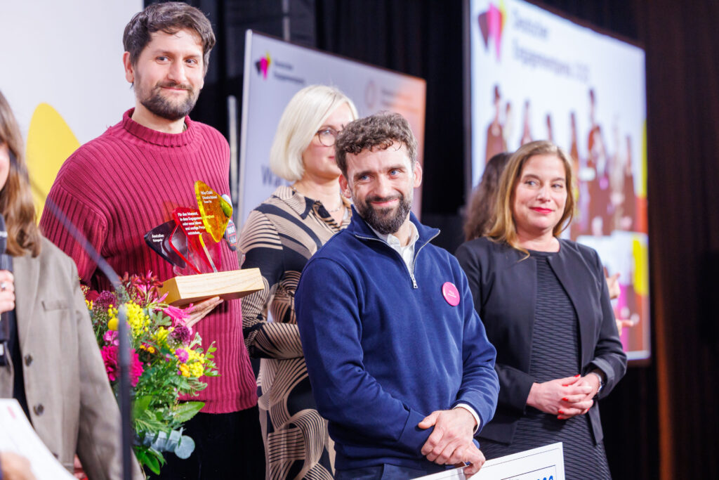 Preisträger und Preisträgerinnen auf der Bühne mit der Trophäe in der Hand