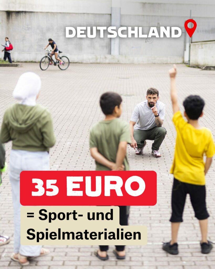 Fünf Kinder stehen auf einem gepflasterten Platz in einer Reihe. Zwei haben den Arm gehoben und melden sich. Ihnen gegenüber hockt ein Mann auf dem Boden. Neben ihm steht eine Frau.