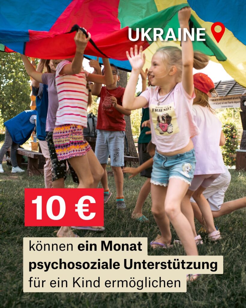 Kinder laufen unter einem großen Bunten Tuch im Kreis. Bildaufschrift: Ukraine: 10 Euro = 1 Monat psychosoziale Unterstützung.