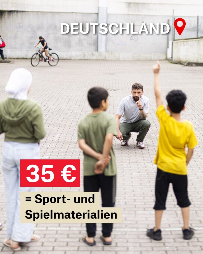 Fünf Kinder stehen auf einem gepflasterten Platz in einer Reihe. Zwei haben den Arm gehoben und melden sich. Ihnen gegenüber hockt ein Mann auf dem Boden. Neben ihm steht eine Frau.