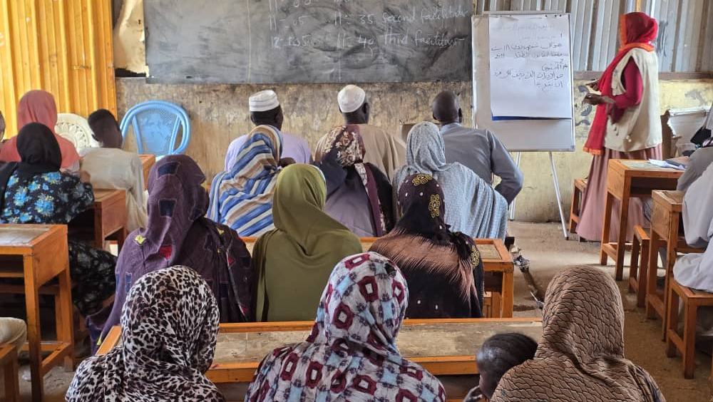 Ein Klassenraum wird gezeigt in dem viele Erwachsene sitzen.