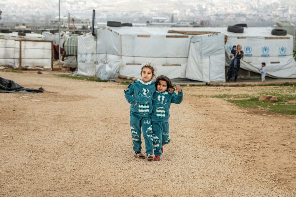 Zwei kleine Kinder stehen Arm in Arm vor einem Flüchtlingslager im Libanon.
