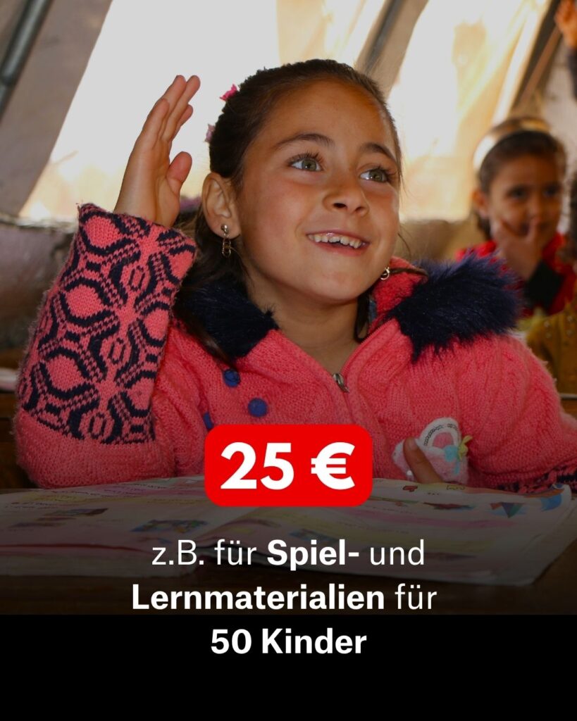 EIn Mädchen mit braunen Haaren und einer Pinken Jacke sitzt am Tisch und meldet sich.