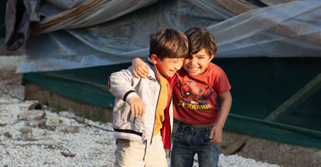 Zwei Jungen lachen arm. in Arm gemeinsam in einem Flüchtlingslager.